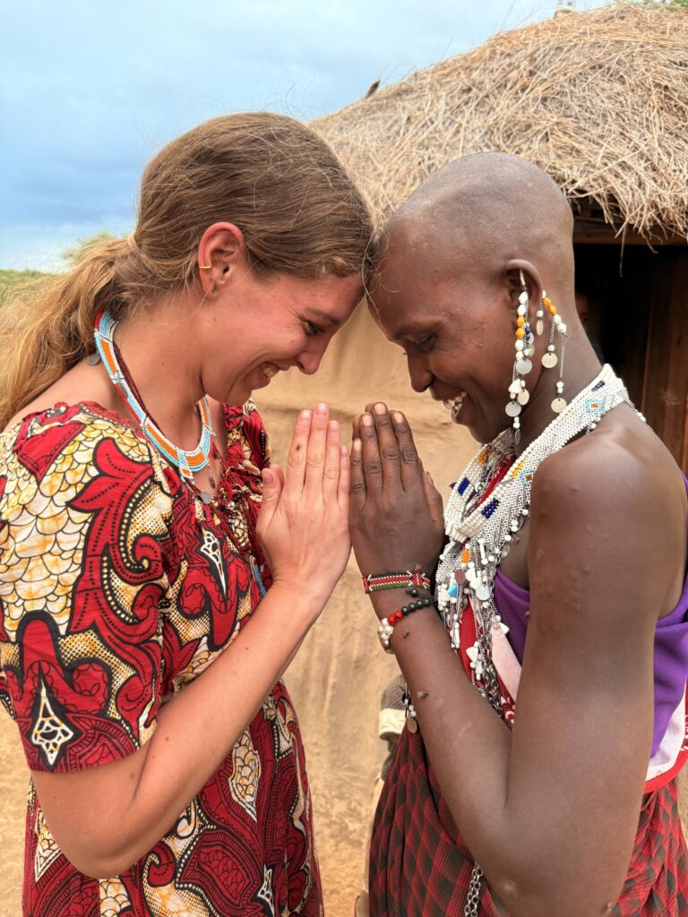 Two women smiling with their foreheads and hands gently pressed together in a warm moment of connection.